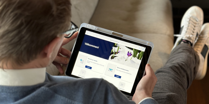 En man ligger i soffan och tittar på en digital skärm som visar Mina sidor