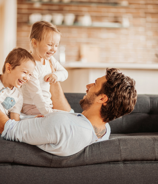 En pappa ligger i soffan och håller i två barn