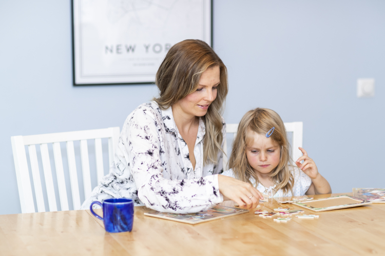 Mamma och dotter sitter vid köksbord och lägger pussel