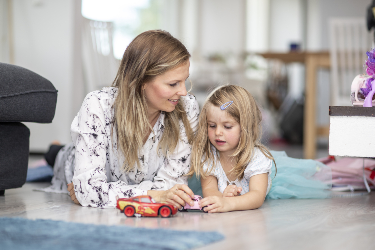 Mamma och barn ligger på golvet med en leksaksbil