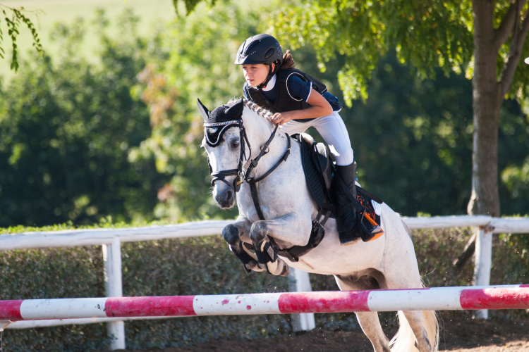 Flicka hoppar över ett hinder med sin häst
