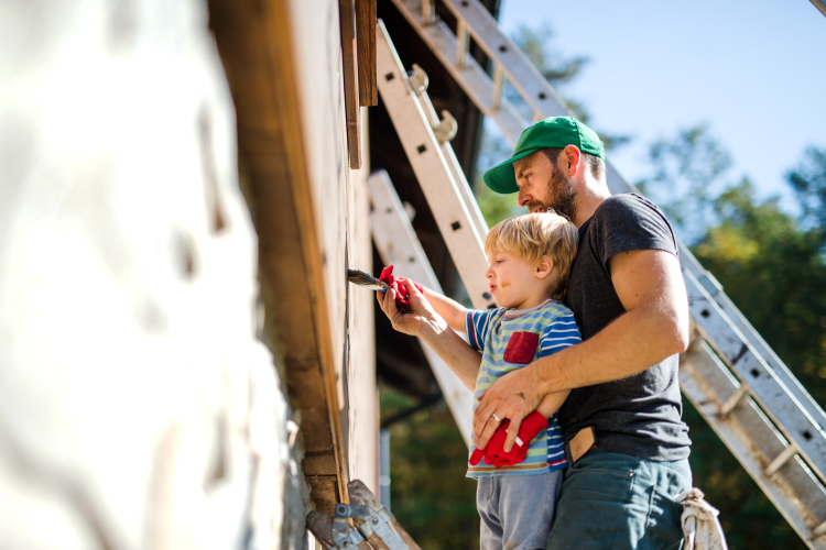 Man och ett barn står och målar ett hus