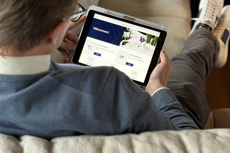En man ligger i soffan och tittar på en digital skärm som visar Mina sidor