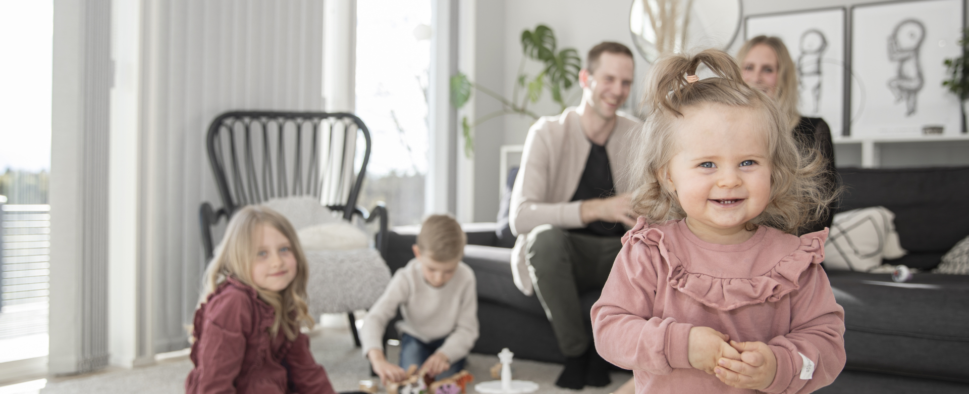 Mamma, pappa och tre små barn umgås i ett vardagsrum