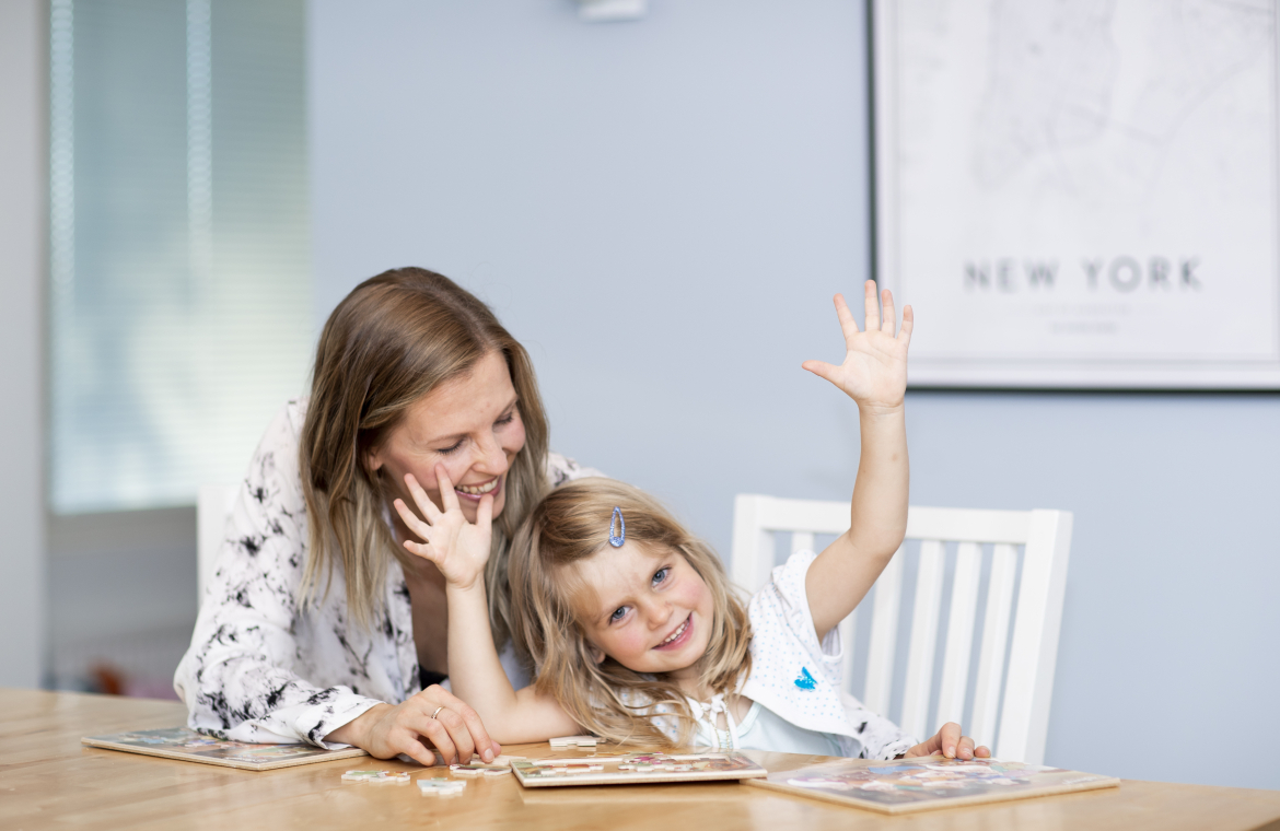 Mamma och liten flicka sitter och pusslar och skojar vid ett matbord