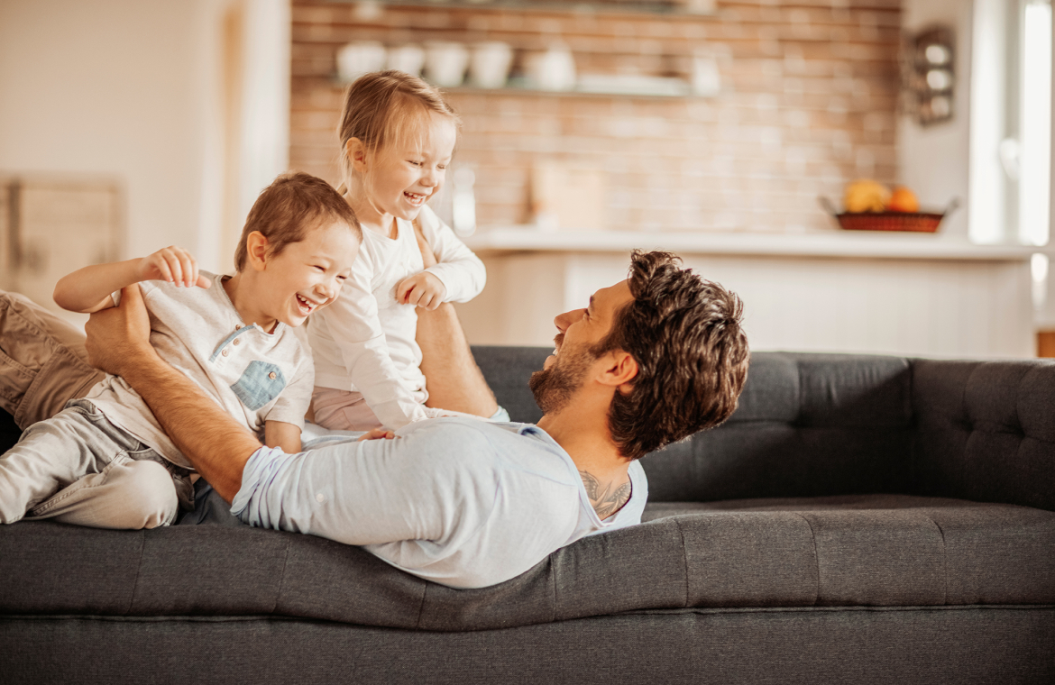 En pappa ligger i soffan och håller i två barn