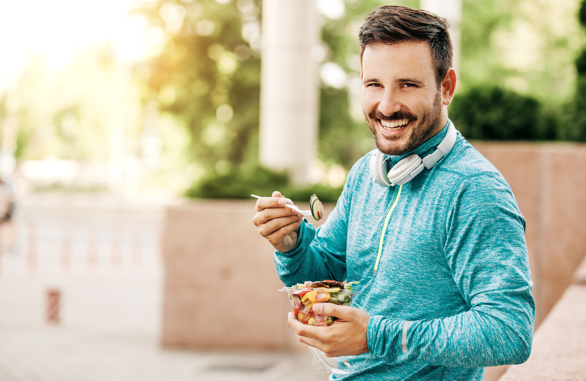 Glad man står med en skål frukt i sin hand